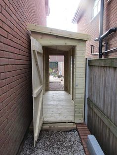 an open door leading to a small wooden shed on the side of a brick building