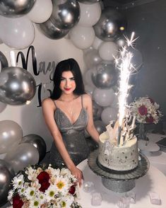 a woman standing in front of a cake with sparklers on it, surrounded by balloons and flowers