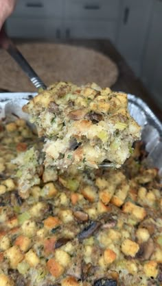 a person is holding a spoon over a casserole dish with stuffing and vegetables