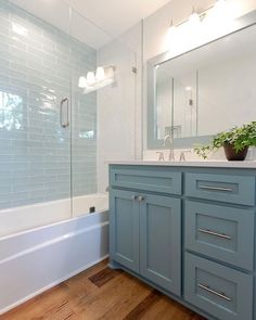 a bathroom with blue cabinets and a white bathtub next to a wooden flooring