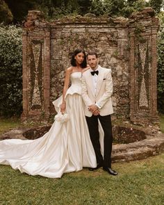 a bride and groom pose for a photo in front of an old stone wall at their wedding