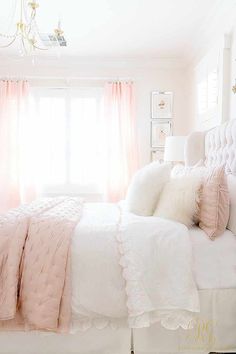 a white bed topped with pillows and pink comforter next to a chandelier