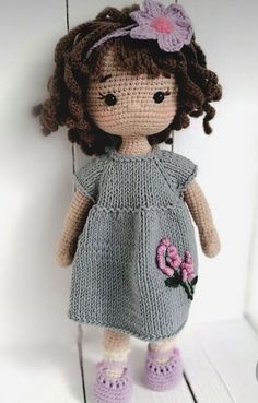 a crocheted doll with brown hair wearing a gray dress and pink flower in her hair