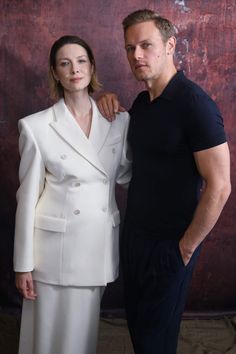 a man and woman standing next to each other in front of a wooden wall wearing white suits