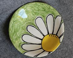 a green and white plate with a flower painted on the front, sitting on a gray surface