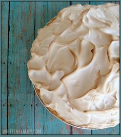 a cake with white frosting sitting on top of a blue wooden table next to a knife