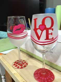 two wine glasses sitting on top of a table next to each other with hearts painted on them