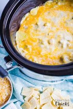 a crock pot filled with cheese and tortilla chips next to other food