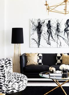 a living room with black and white furniture, gold accents and paintings on the wall