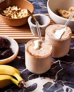 two glasses filled with smoothie next to bananas and raisins on a table