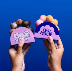 two hands holding up small boxes with donuts in front of them and the words club mochi written on top