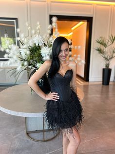 a woman standing in front of a table wearing a black feathered dress and heels