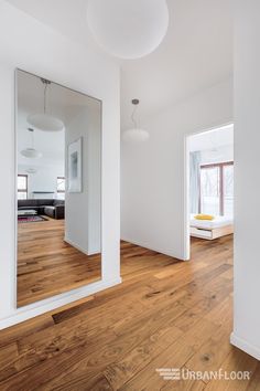 an empty room with wood flooring and white walls is seen through a large mirror