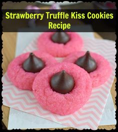 three pink cookies with chocolate on top sitting on a wooden board next to candy candies