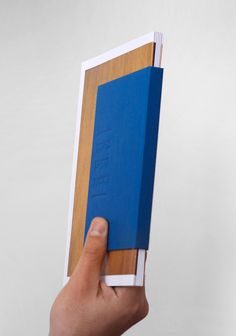 a hand holding a blue book in front of a white wall