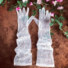 two white gloves with pearls on them next to flowers