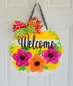 a welcome sign hanging on a door with polka dots and flowers painted on the front