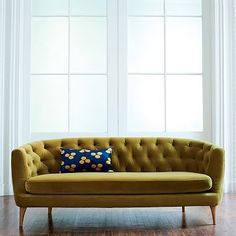 a yellow couch sitting in front of a window next to a wooden floor and white curtains