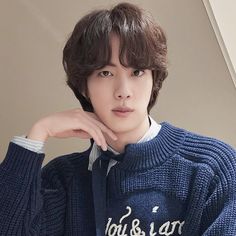 a young man wearing a blue sweater with his hand on his chin and looking at the camera