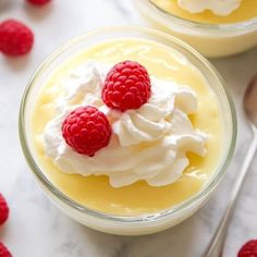 two desserts with whipped cream and raspberries in small bowls on a marble surface