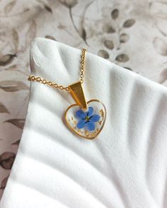 💙 This heart pendant features a delicate forget-me-not flower encased in UV resin, creating a charming necklace with tiny blue flowers. The gold-plated stainless steel adds a touch of elegance to the design, making it a sweet and thoughtful handmade gift for a daughter. Perfect for girls, this cute piece of jewelry blends natural beauty with a timeless style. ⭐ Please note that this item is made to order, and the details may slightly differ from the photos as it is a handmade and unique product Pendant Delicate, Jewelry For Girls, Forget Me Not Flower, Flowers Cute, Gift For Daughter, Gold Flakes, Forget Me Not, Uv Resin, Handmade Pendant