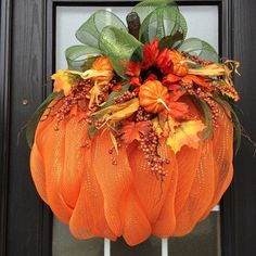 an orange mesh wreath with leaves and flowers on the front door handle, hanging from a black wooden door