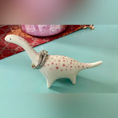 Keep Your Rings Close And Secure With This Adorable Ceramic Dino Ring Holder. Features Adorable Pink Hearts As Its Spots! Rings Can Be Placed On Both The Neck And Hung From The Tail. Well, Smaller Rings Fit On The Tail The Best. Keep This Smiling Buddy On Your Dresser, Nightstand, Or Vanity As A Convenient Way To Keep Your Precious Jewelry Safe. Measures Approximately 5” In Length, 3.5” In Height, And Just Under An Inch Across The Widest Area Of Its Back. Seems Large When Thinking Of It In These Dog Pottery Ring Holder, Dinosaur Ring Holder, Dino Ring, Cactus Ring Holder Clay, Cute Ceramic Ring Holder, Cactus Ring Holder, Dresser Nightstand, Jewelry Safe, Pink Hearts