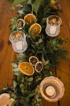 an arrangement of oranges and candles on a table with greenery, leaves and flowers