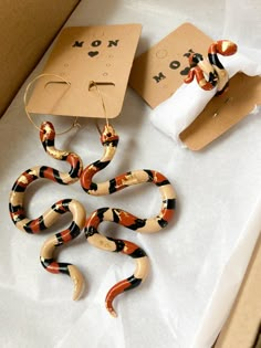 a pair of snake shaped earrings sitting on top of a white table next to a roll of toilet paper