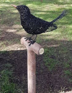 a wire bird sitting on top of a wooden post in the grass next to a tree