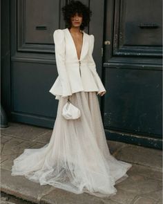 a woman standing in front of a black door wearing a white dress and blazer