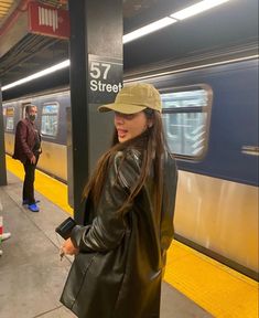 a woman wearing a hat standing next to a train at a subway station with people waiting on the platform