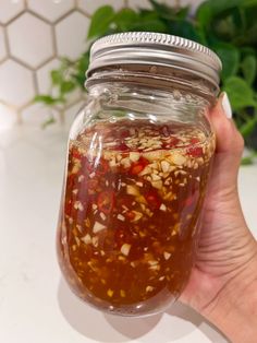 a person holding a jar filled with food on top of a white counter next to a plant