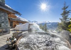 an outdoor hot tub in front of a building with snow on the mountains behind it