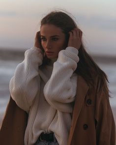 a woman with long hair wearing a coat and holding her hand up to her ear