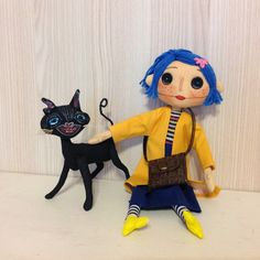 a doll with blue hair sitting next to a black cat