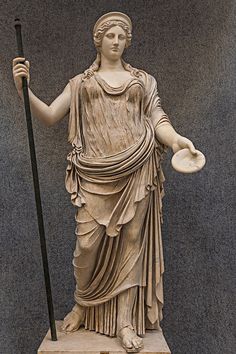 a statue of a woman holding a hat and a cane in one hand, standing on a pedestal