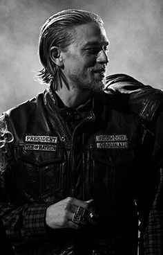 a black and white photo of a man wearing a leather jacket with patches on it