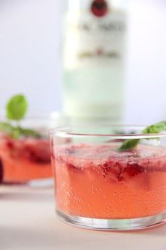 two glasses filled with drinks sitting on top of a white table next to a bottle