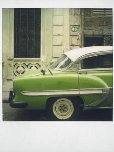 an old green car parked in front of a building