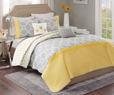 a bed with yellow and gray comforters in a bedroom next to windows, rugs and curtains