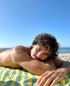 a man laying on top of a yellow and green towel next to the ocean with his hand under his chin