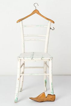 a white chair with a wooden hanger on it's back and an old pair of shoes underneath