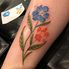 a blue and orange flower tattoo on the leg with green leaves in front of it