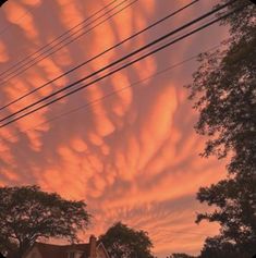 the sky is filled with pink clouds and some power lines in front of a house