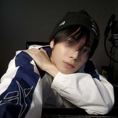 a young man sitting in front of a keyboard wearing a black beanie and looking at the camera