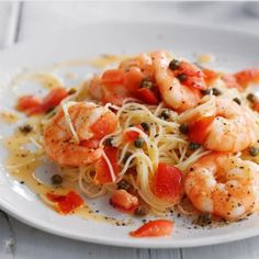 a white plate topped with pasta and shrimp on top of a bed of tomato sauce