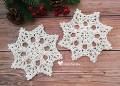 two crocheted snowflakes sitting on top of a wooden table next to pine cones