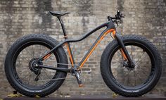 an orange and black mountain bike parked in front of a brick wall