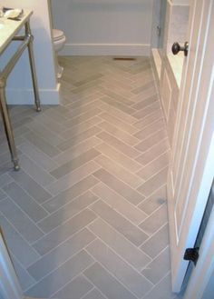 a bathroom with a toilet, sink and herringbone tile flooring in the shower